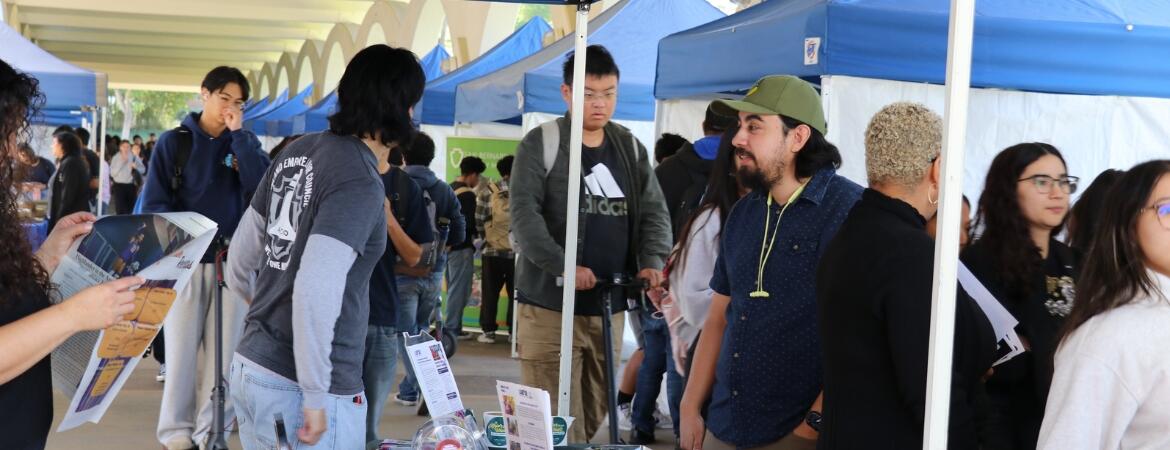 Group of UCR students, staff, faculty, and community members under the Rivera arches, visiting booths