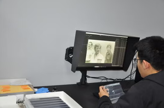 A person sits in front of a box of slides and a computer with a black and white image on the screen.