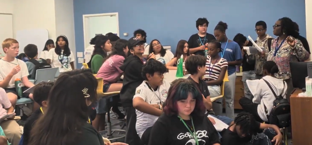 Middle school students are in a classroom listening to a teacher
